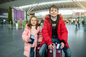 happy cheerful european kids boy and girl in warm clothes sitting on a suitcase and holding passports with air tickets and boarding pass at the international airport family airplane travel concept