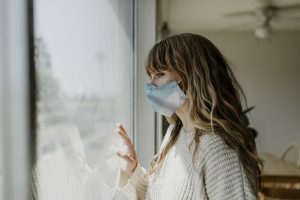 mulher usando uma mascara olhando pela janela durante um bloqueio 1