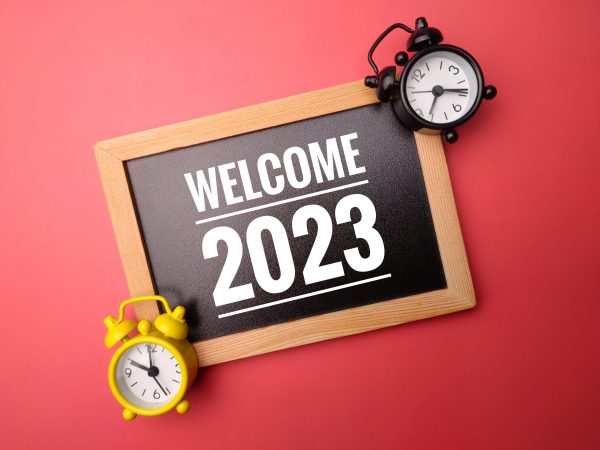 wooden frame and alarm clock with the word welcome 2023 on red background